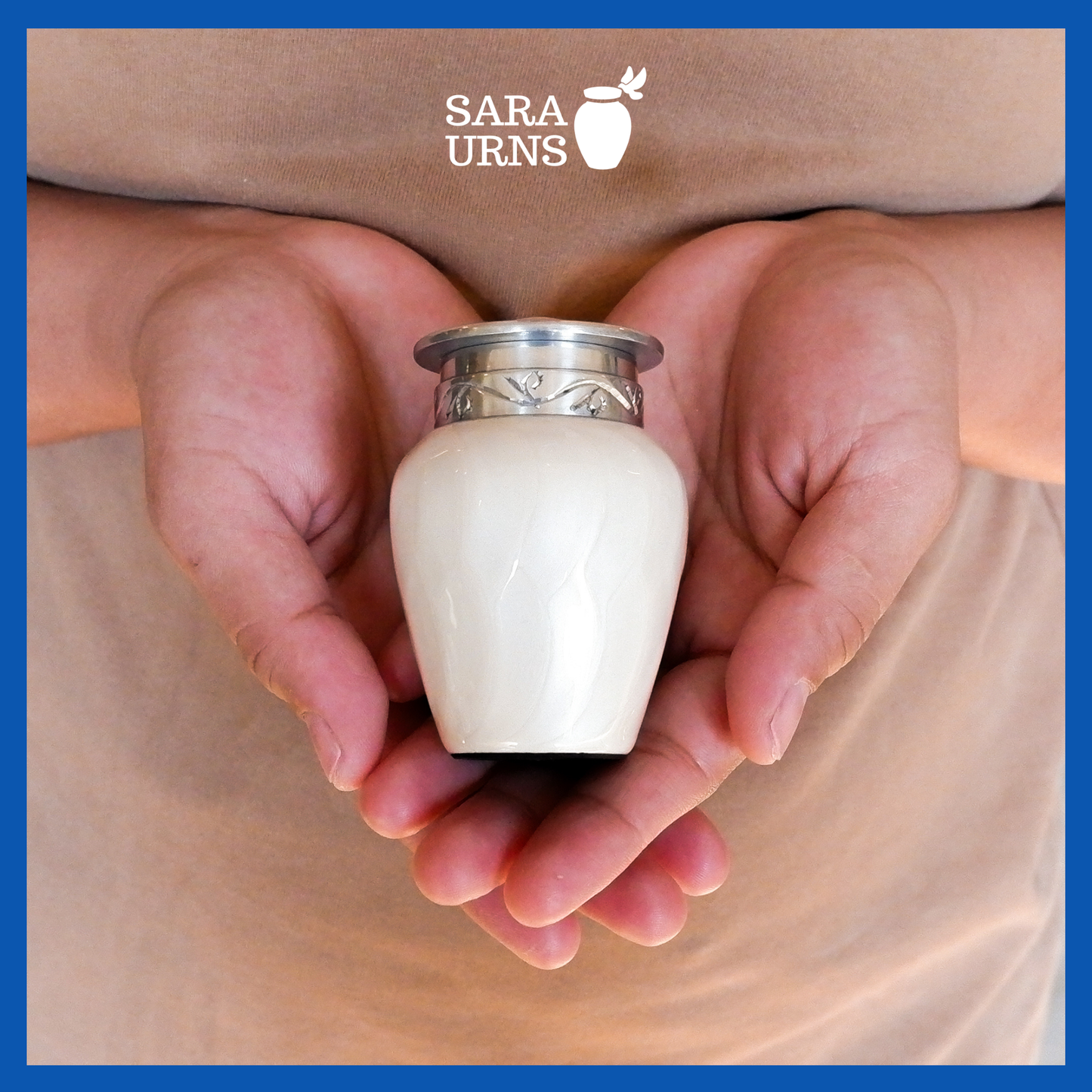 A presentation of a white aluminum metal keepsake urn with a silver hand-etched design held by an adult woman with two hands.