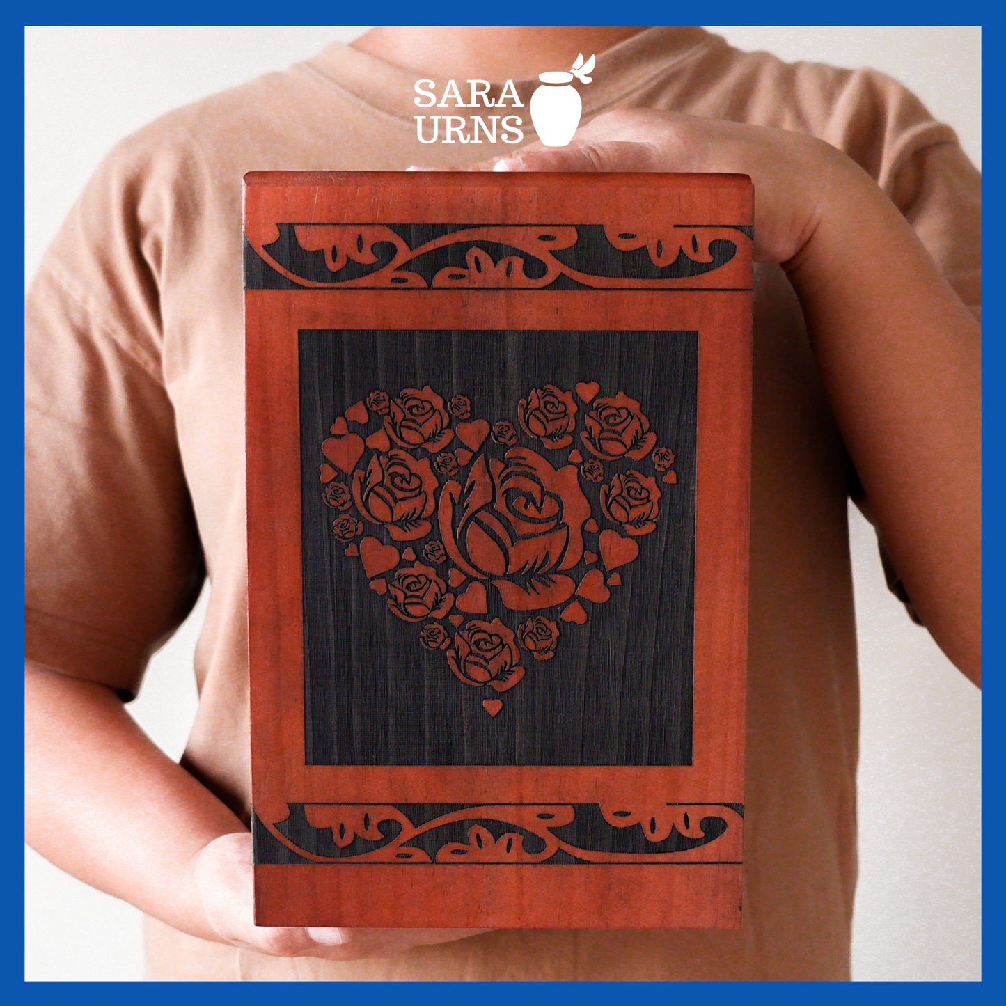 A presentation of a terracotta pine wooden urn with an intricate engraving of roses within a heart held by an adult woman with two hands.