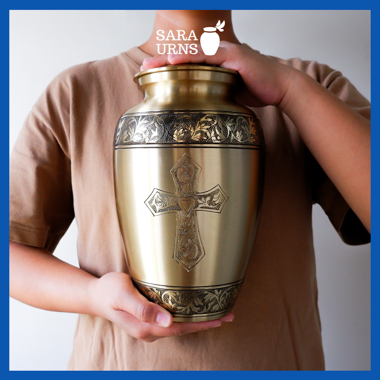 A gold polished brass metal urn with a hand-etched holy cross held by an adult woman with two hands.