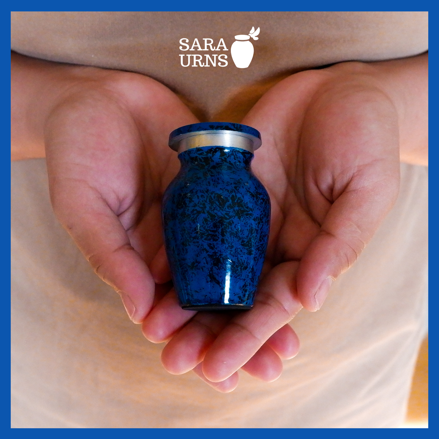 An all-blue aluminum metal keepsake urn with a black speckled pattern across the body and lid held by an adult woman with two hands.