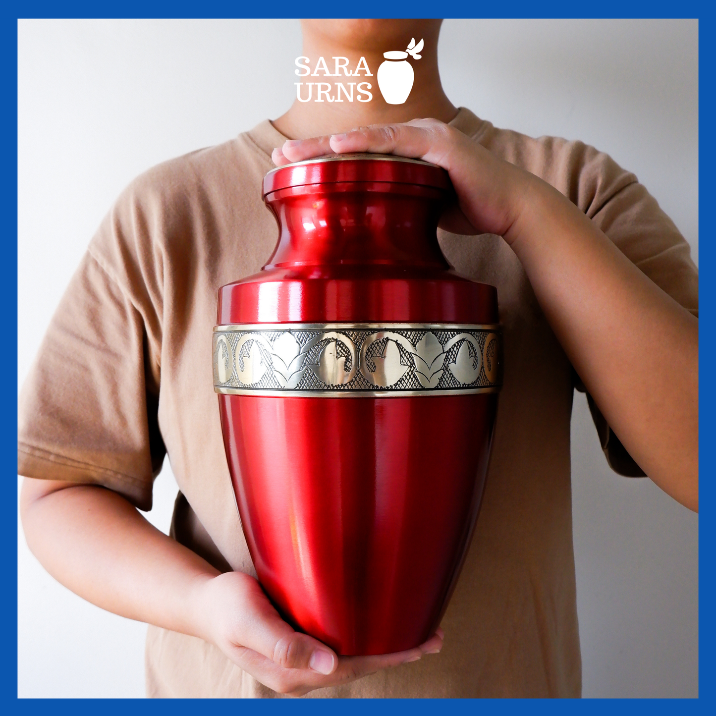 A presentation of a red polished brass metal urn with golden hand-etched details across the lid and body held by an adult woman with two hands.