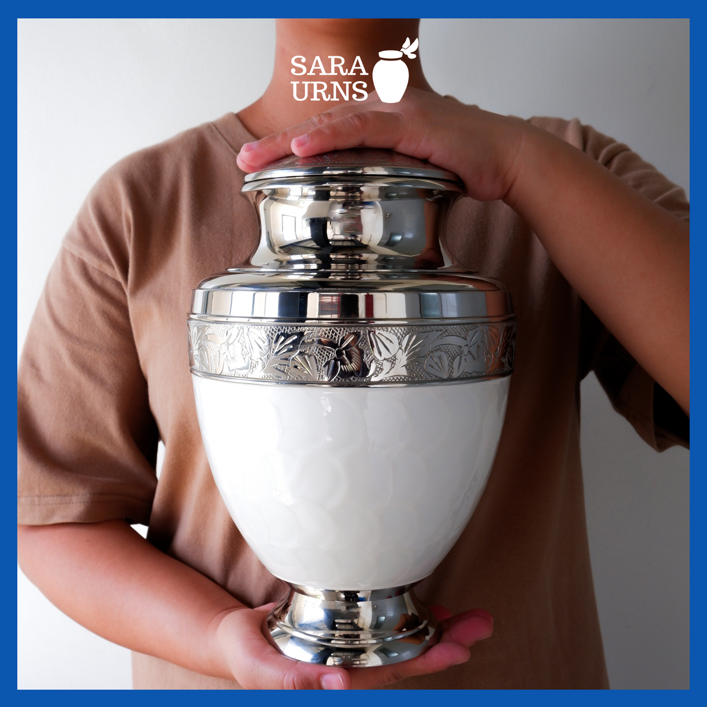 A presentation of a white polished brass metal urn held by an adult woman with two hands.