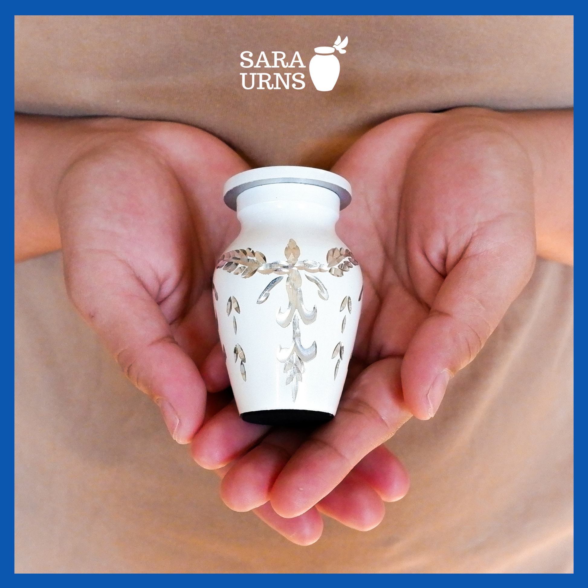A presentation of a white aluminum metal keepsake urn with an engraved gem-like design held by an adult woman with two hands.