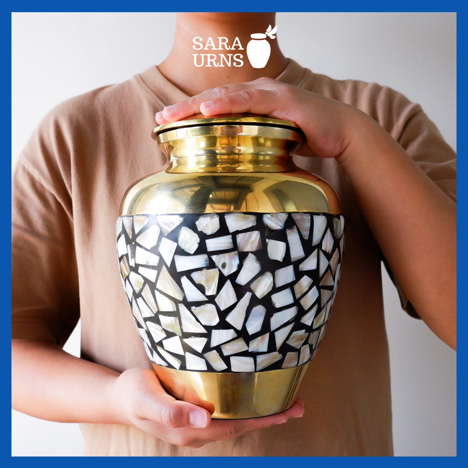A presentation of a golden polished brass metal urn with a shell mosaic design held by an adult woman with two hands.