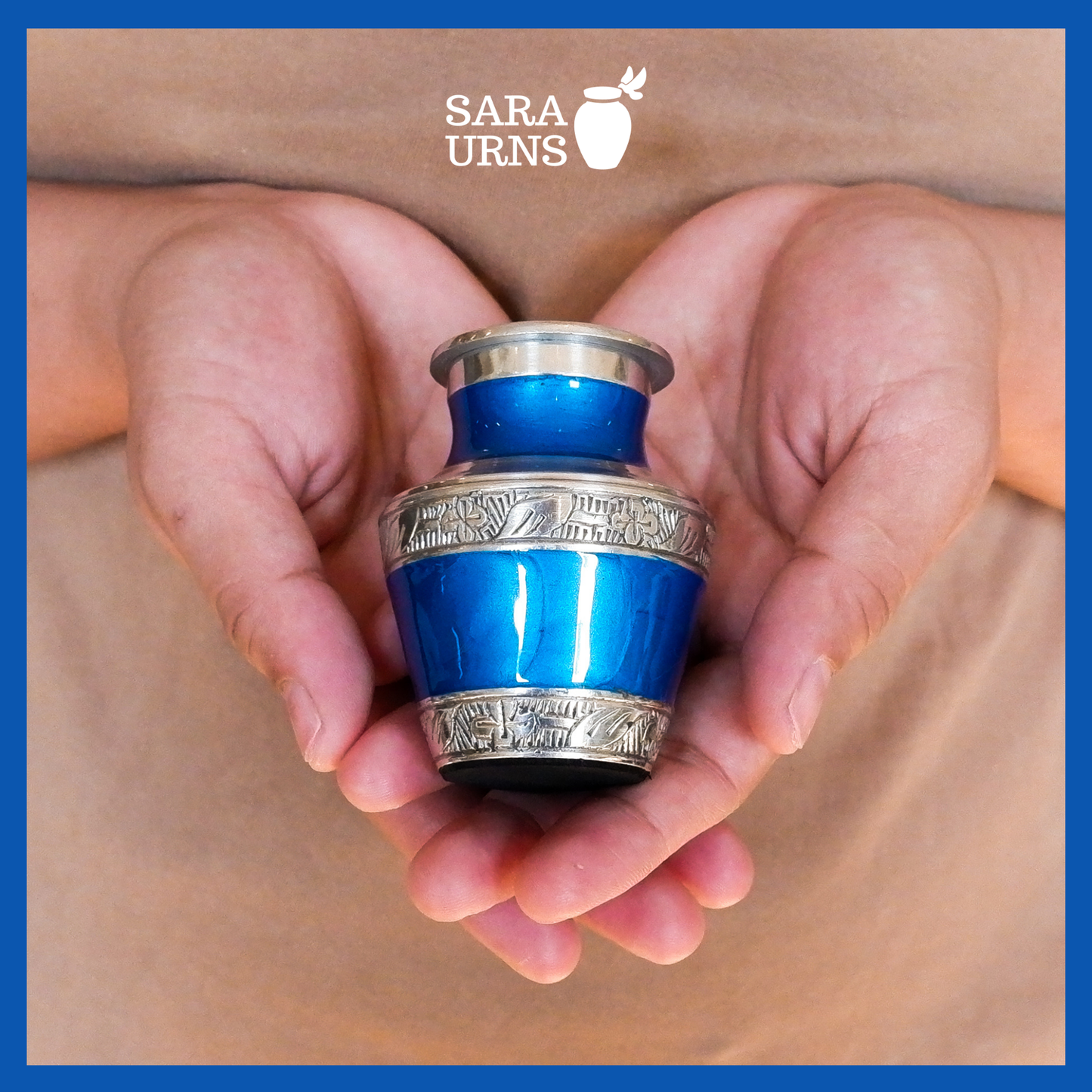 A presentation of a blue aluminum metal keepsake urn with silver hand-etched designs across the body and lid held by an adult woman with two hands.