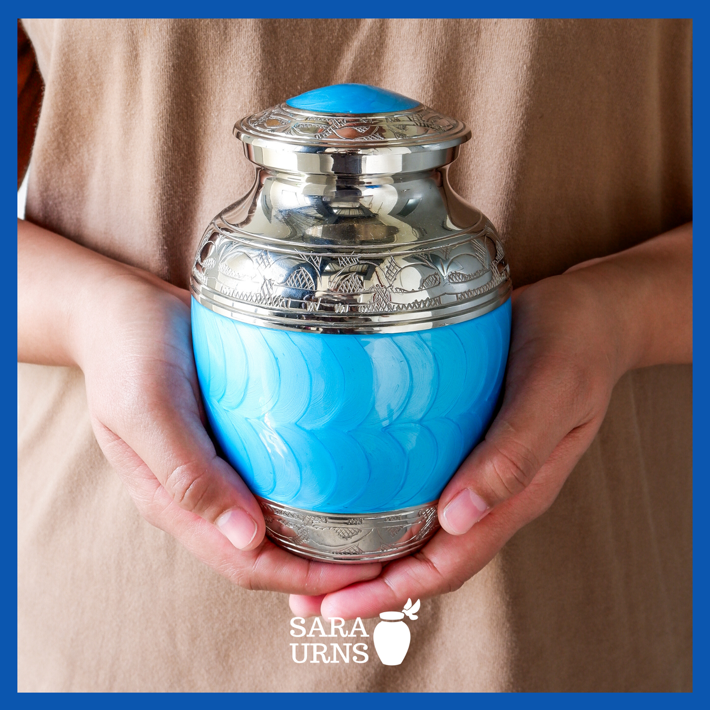 A presentation of a bright blue polished brass metal baby urn held by an adult woman with two hands.