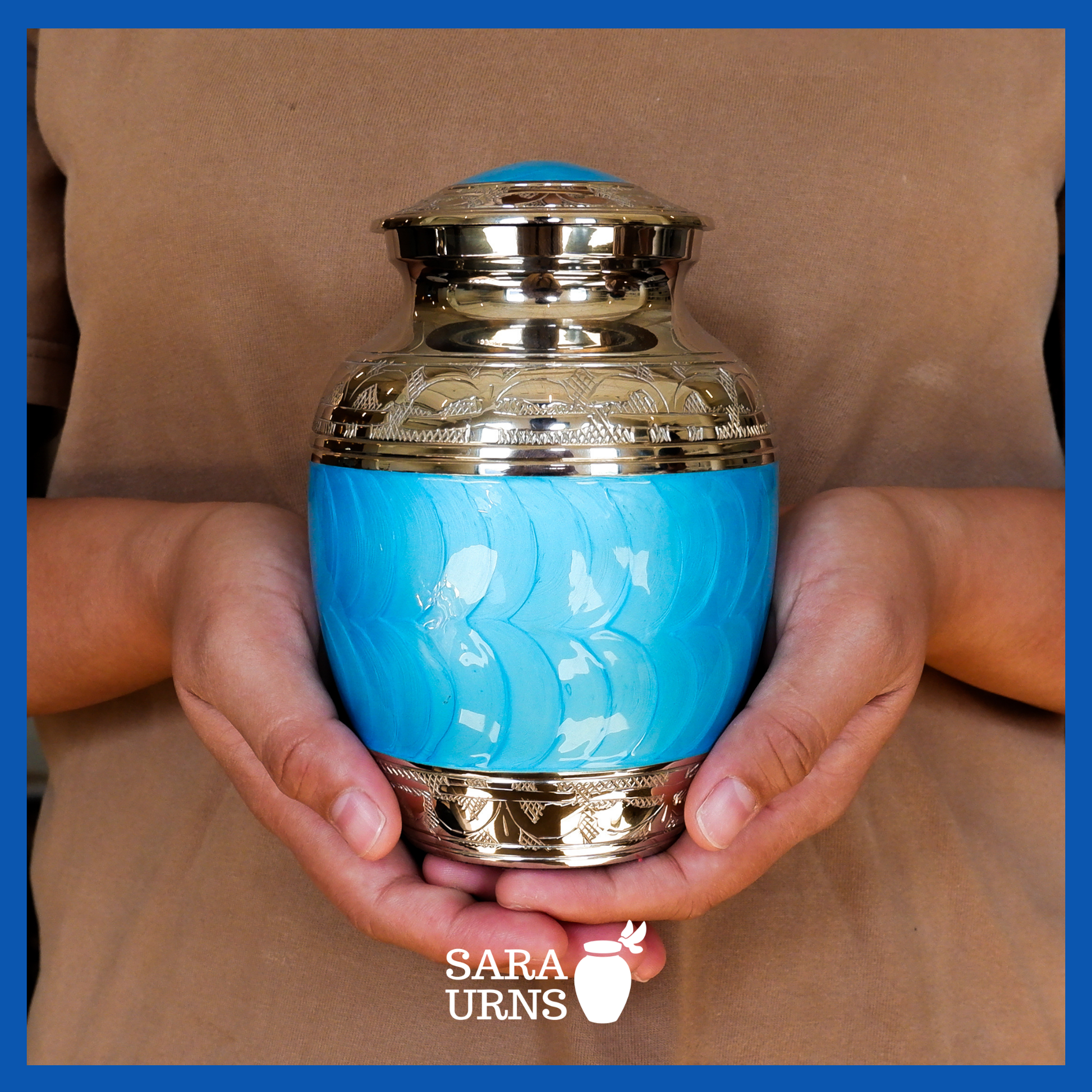 A presentation of a bright blue polished brass metal baby urn held by an adult woman with two hands.