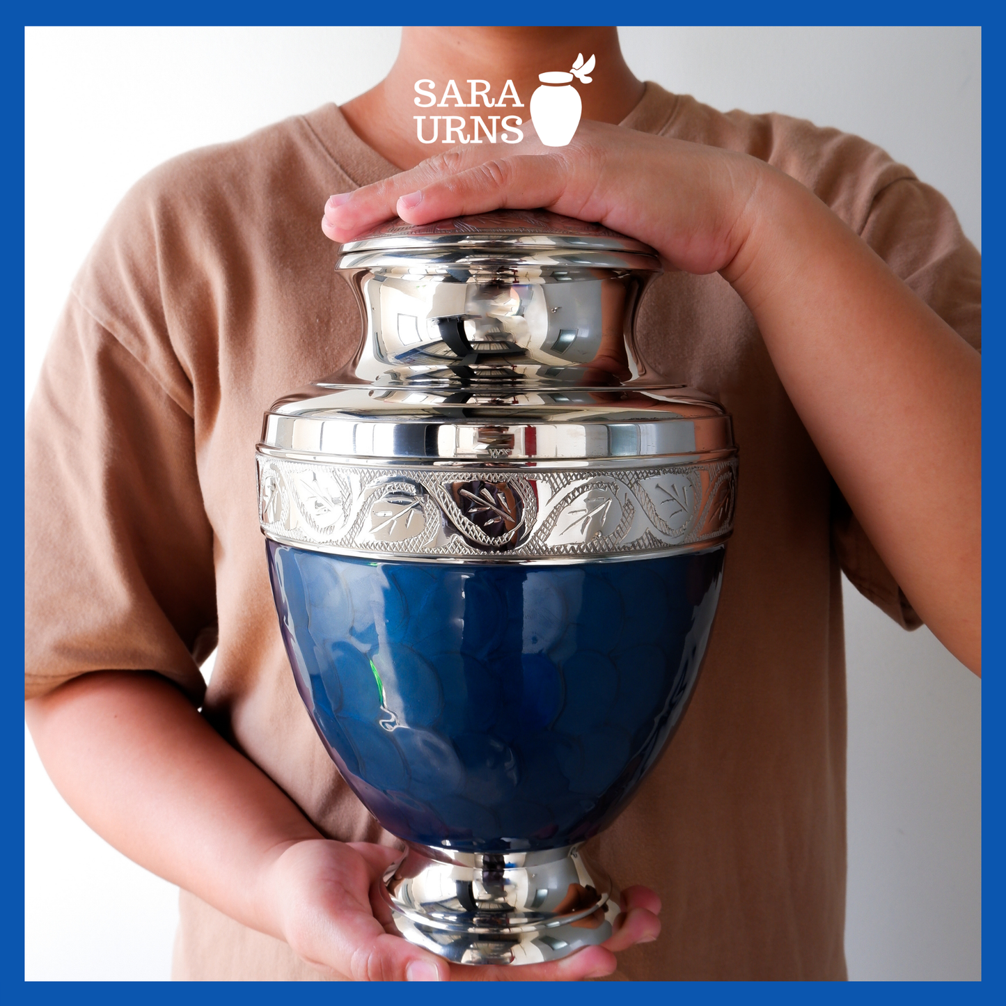 A presentation of a dark blue polished brass metal urn held by an adult woman with two hands.