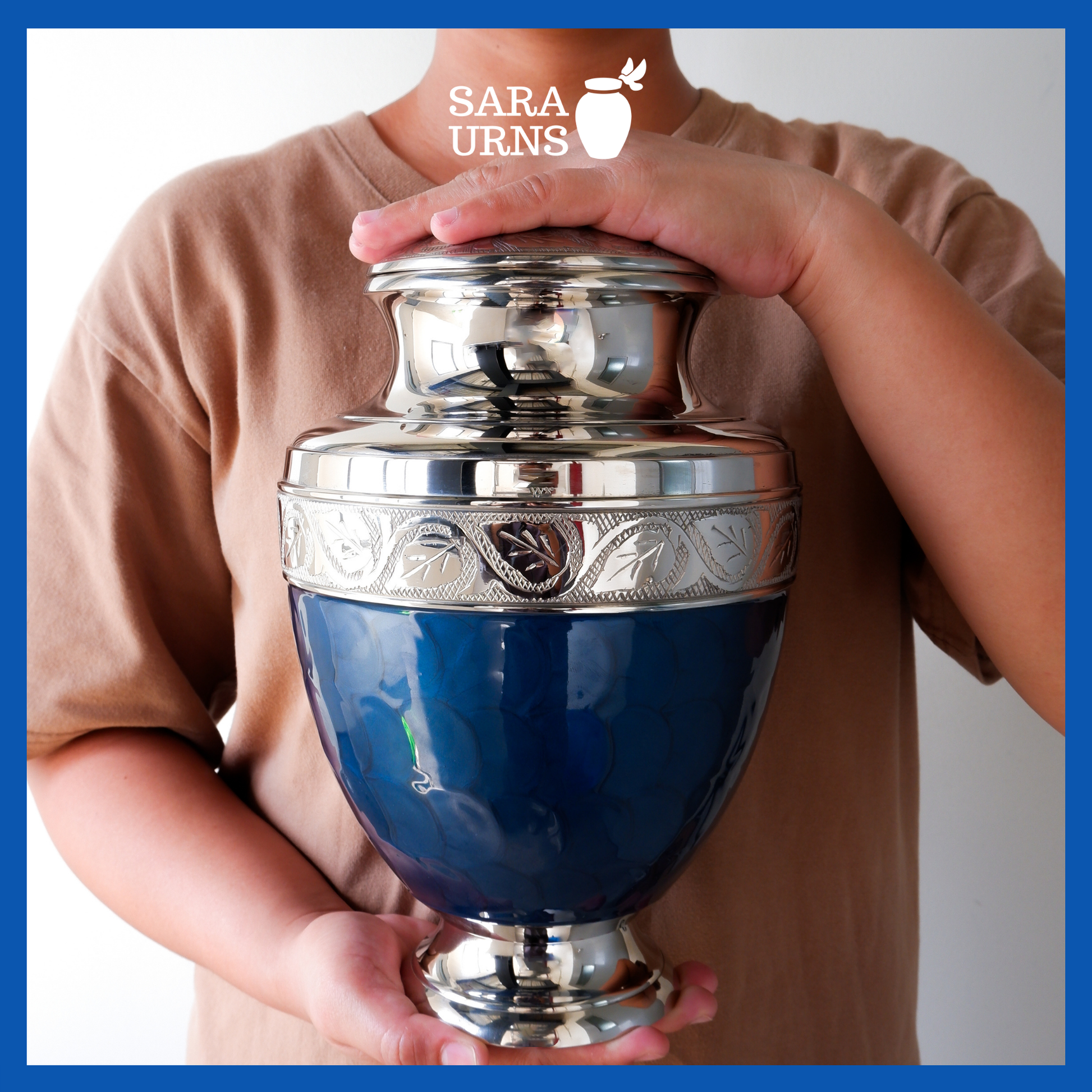 A presentation of a dark blue polished brass metal urn held by an adult woman with two hands.