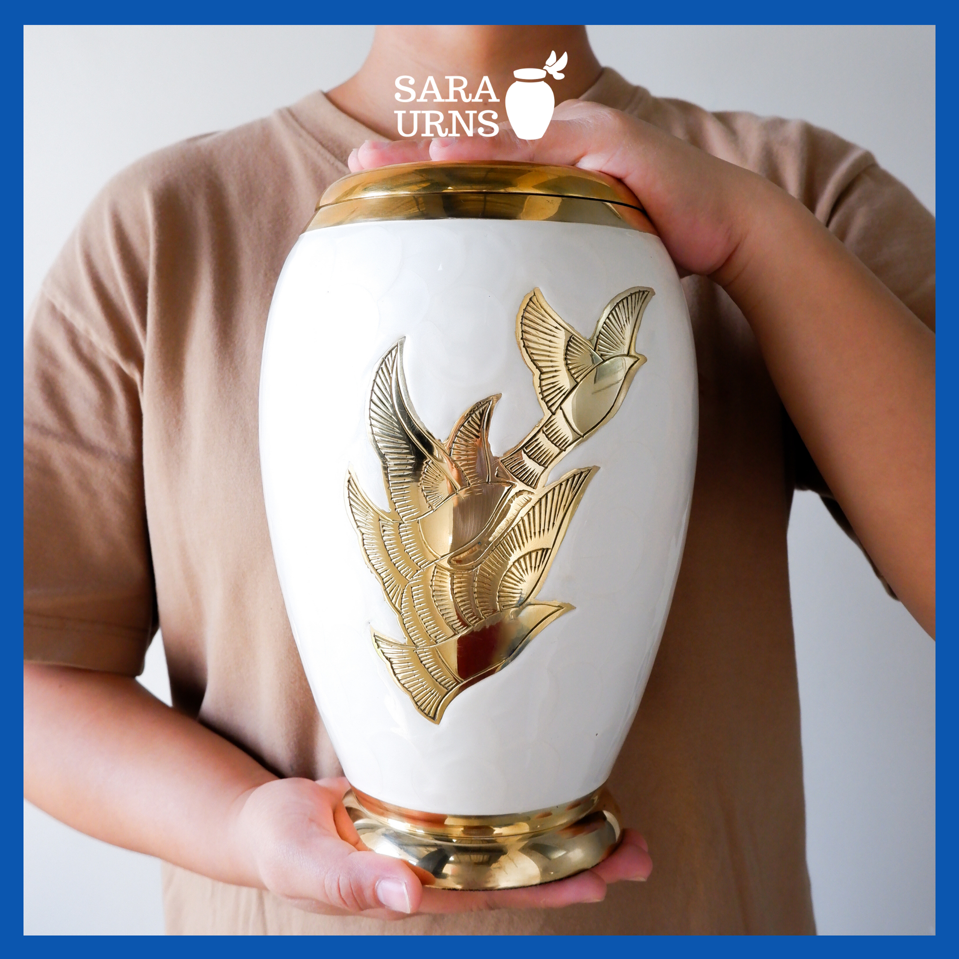 A presentation of a white polished brass metal urn with golden, hand-etched winged doves held by an adult woman with two hands.