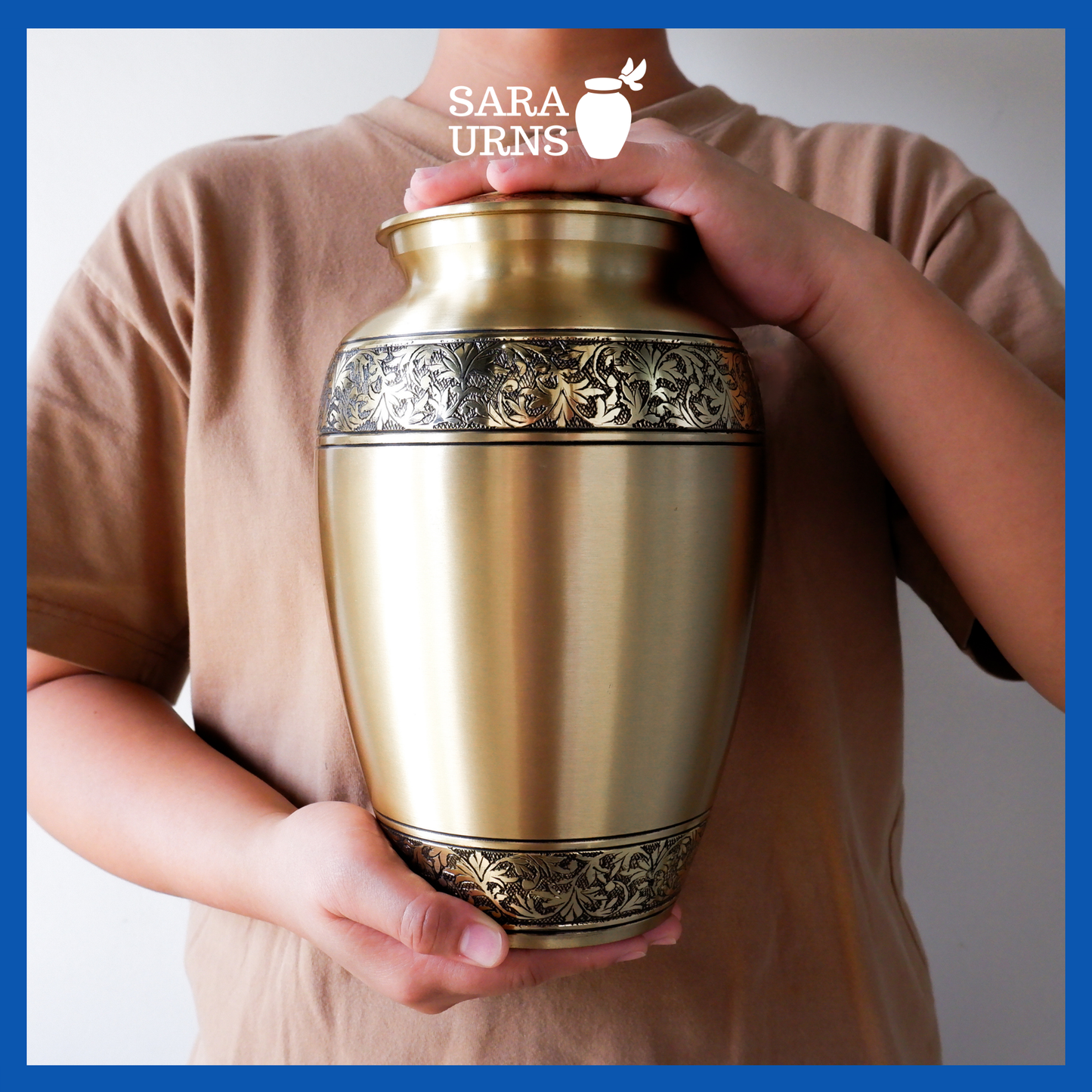 A presentation of a gold polished brass metal urn with hand-etched details on its body and lid held by an adult woman with two hands.