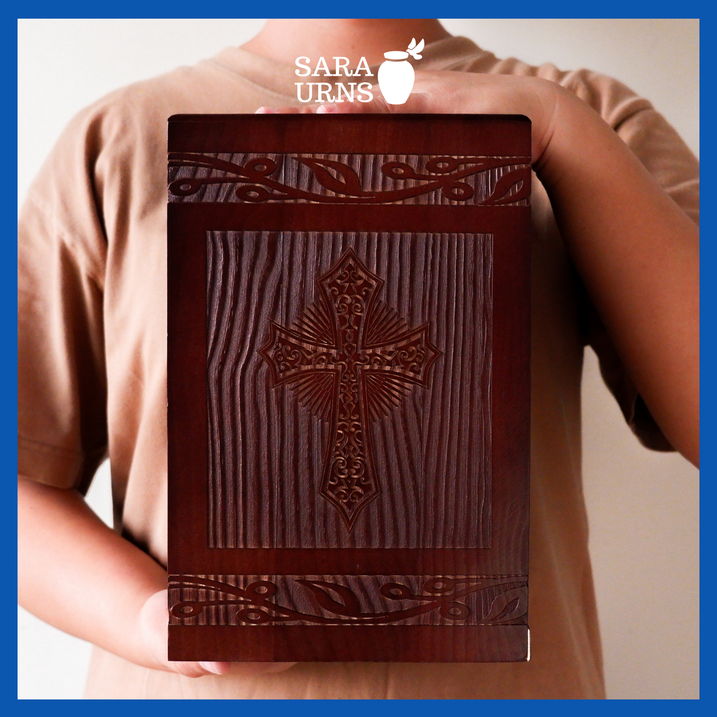 A presentation of a brown pine wooden urn with an intricate engraving of the holy cross held by an adult woman with two hands.