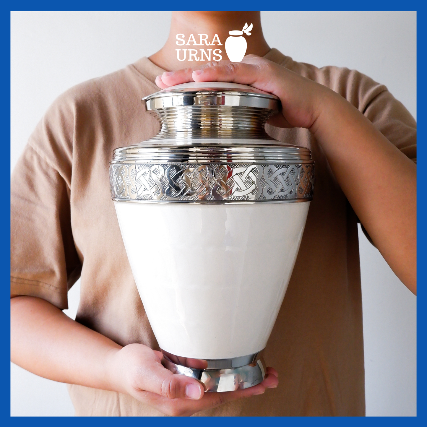 A presentation of a white polished brass metal urn with silver hand-etched knot details held by an adult woman with two hands.