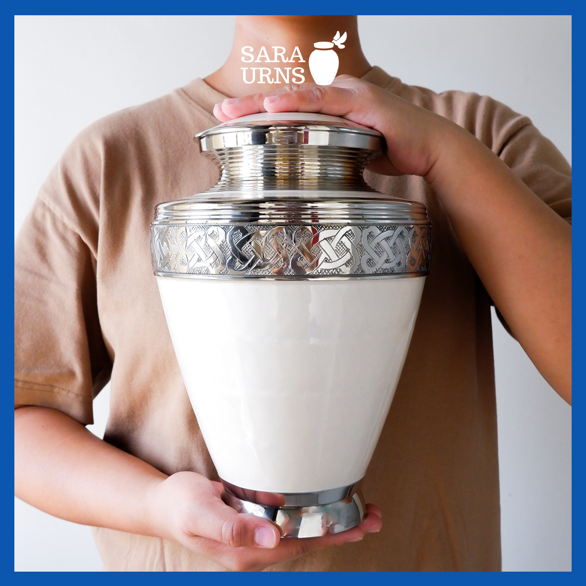 A presentation of a white polished brass metal urn with silver hand-etched knot details held by an adult woman with two hands.