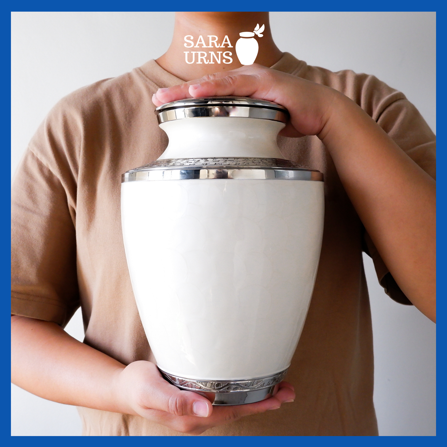 A presentation of a white polished brass metal urn with an enamel finish and hand-etched details held by an adult woman with two hands.