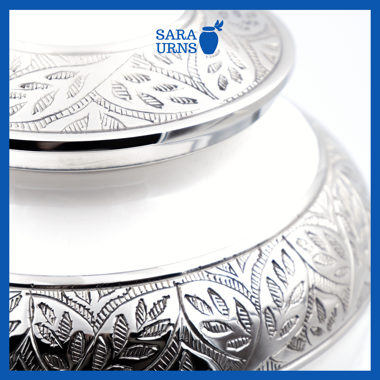 A close-up angle of a white polished brass metal urn with an enamel finish which highlights its silver hand-etched details.