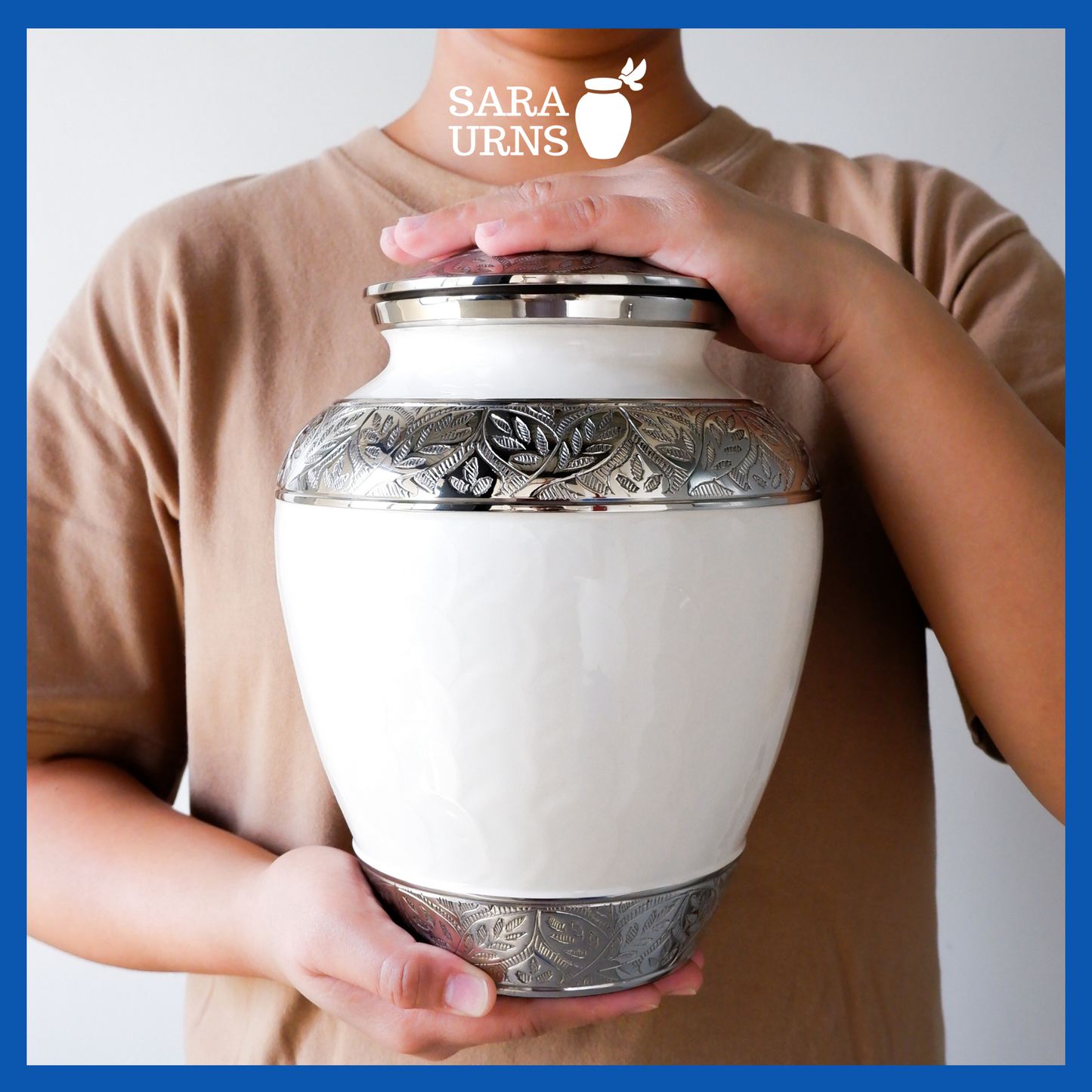 A presentation of a white polished brass metal urn with an enamel finish and hand-etched details held by an adult woman with two hands.