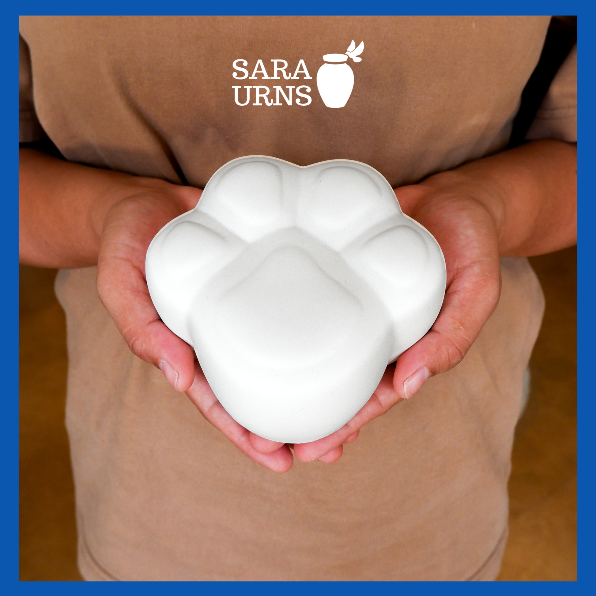A presentation of a paw-shaped, white ceramic pet urn held by an adult woman with two palms.