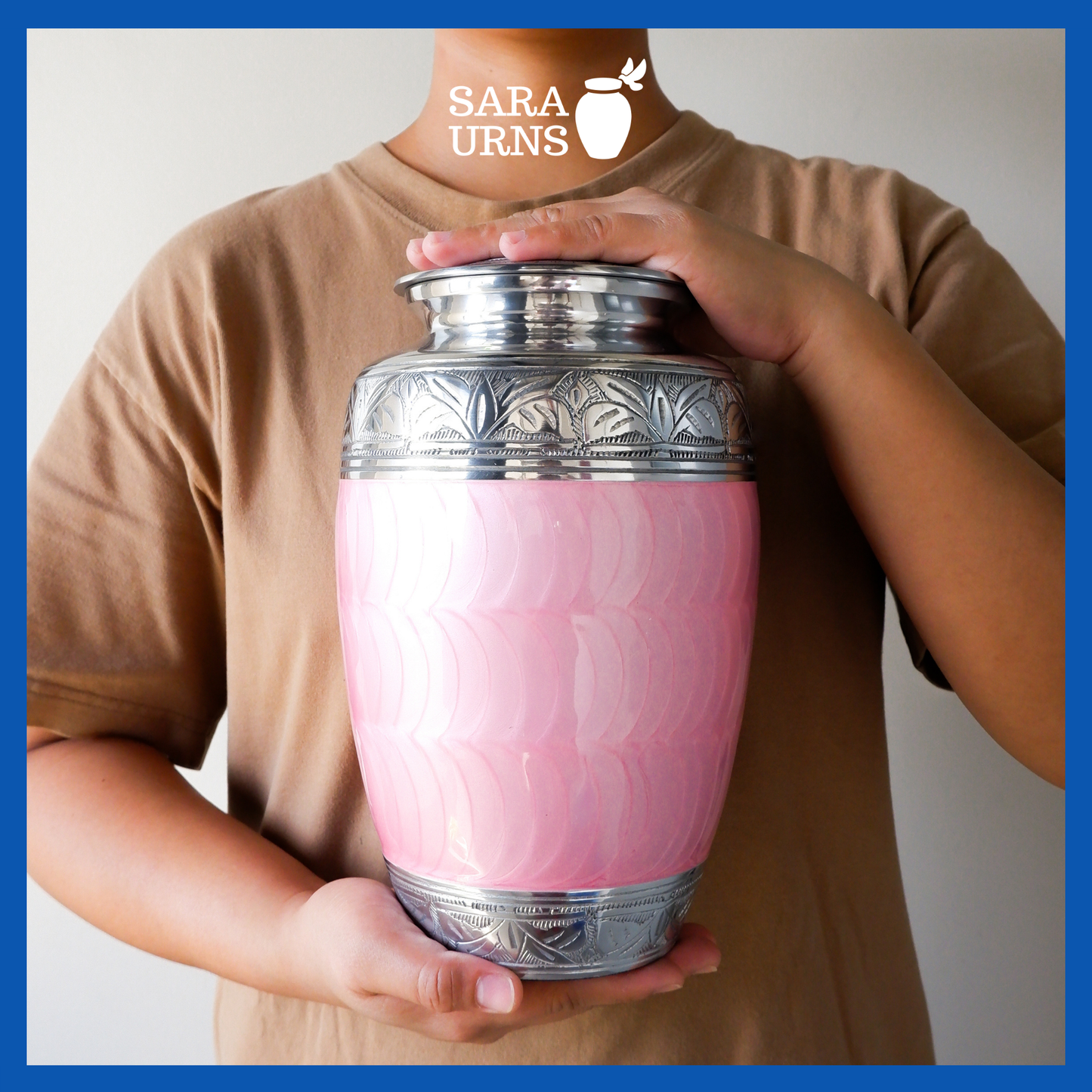 A presentation of a pink polished aluminum brass metal urn with an enamel finish and hand-etched details held by an adult woman with two hands.