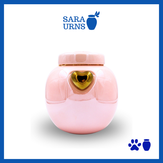 A pink ceramic pet urn with a pearly finish, a gold heart at its center and an embossed paw detail in the lid over a white background.