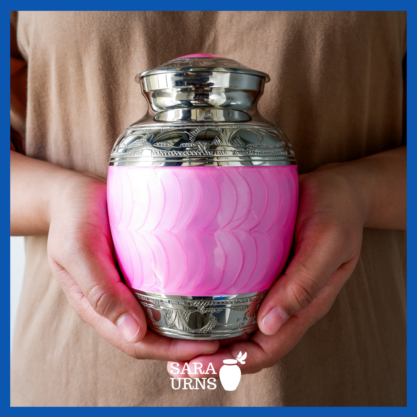 A presentation of a bright pink polished brass metal baby urn held by an adult woman with two hands.
