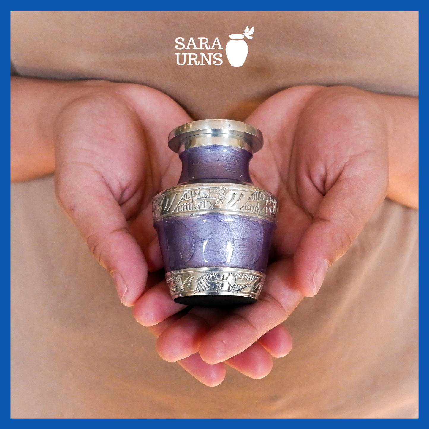A presentation of a purple aluminum metal keepsake urn with silver hand-etched designs across the body and lid held by an adult woman with two hands.