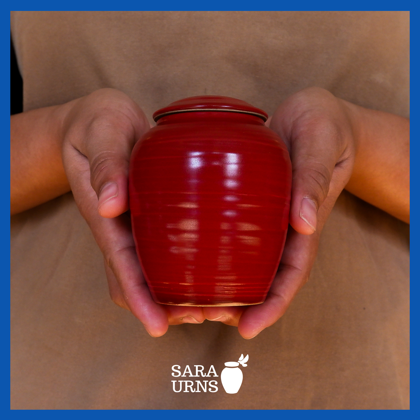 A presentation of a red polished ceramic baby urn held by an adult woman with two hands.