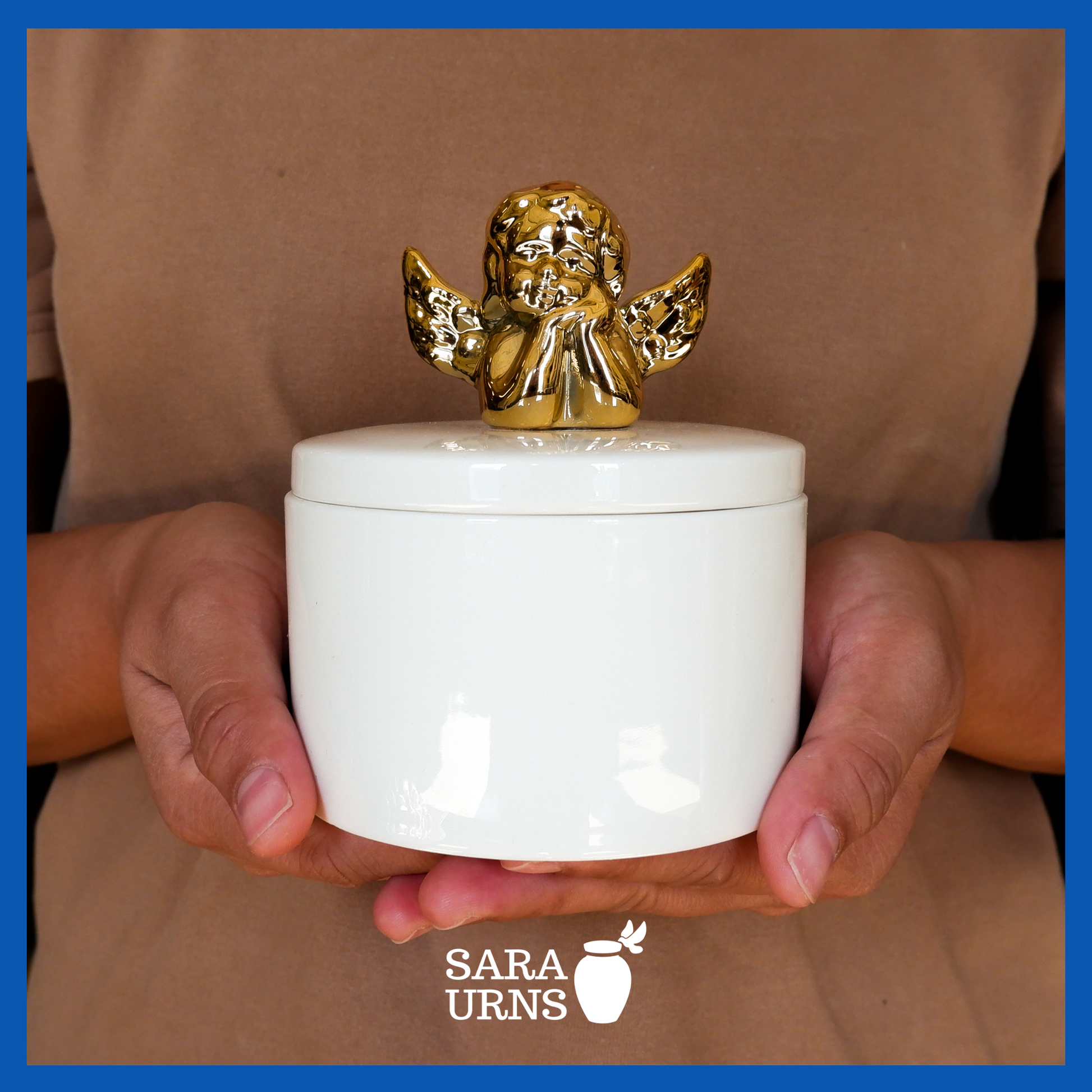 A presentation of a white polished ceramic baby urn with a golden cherub on its lid held by an adult woman with two hands.