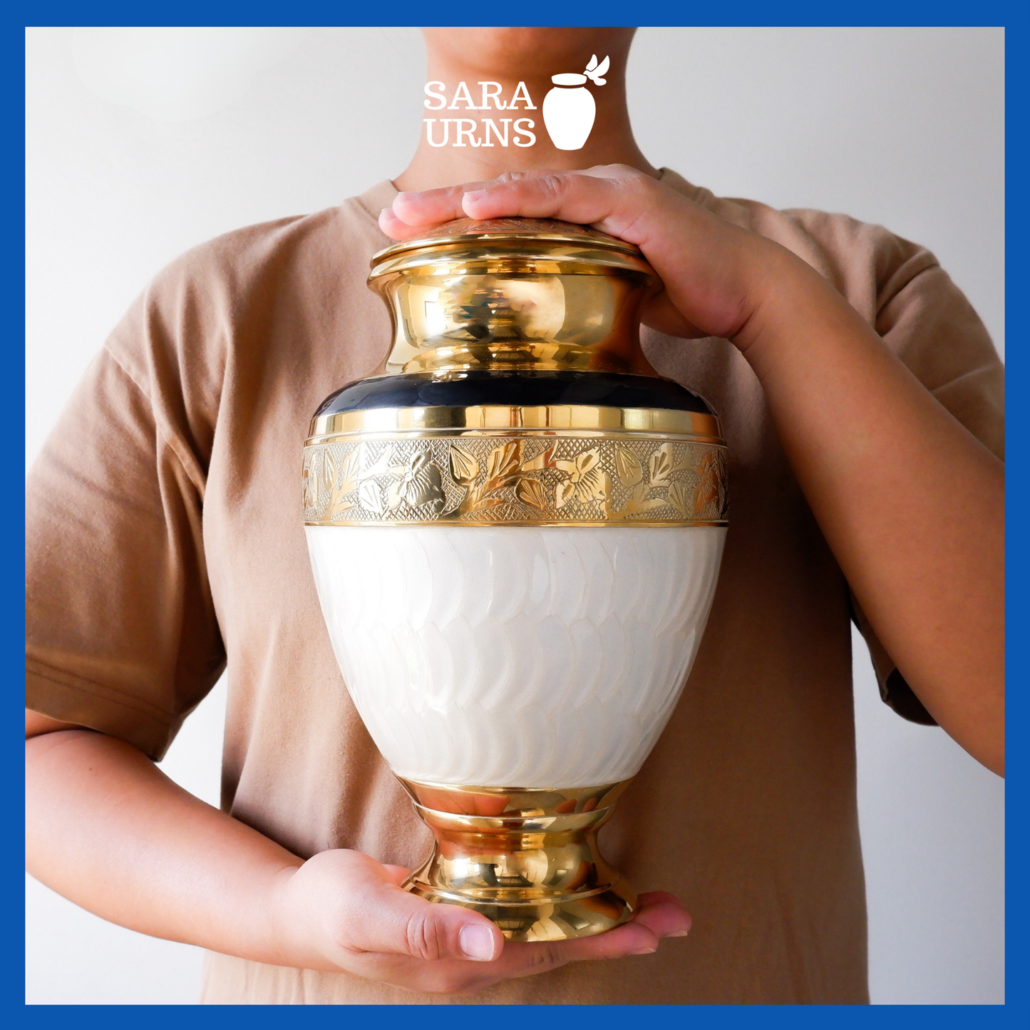 A white polished brass metal urn with golden, hand-etched details held by an adult woman with two hands.