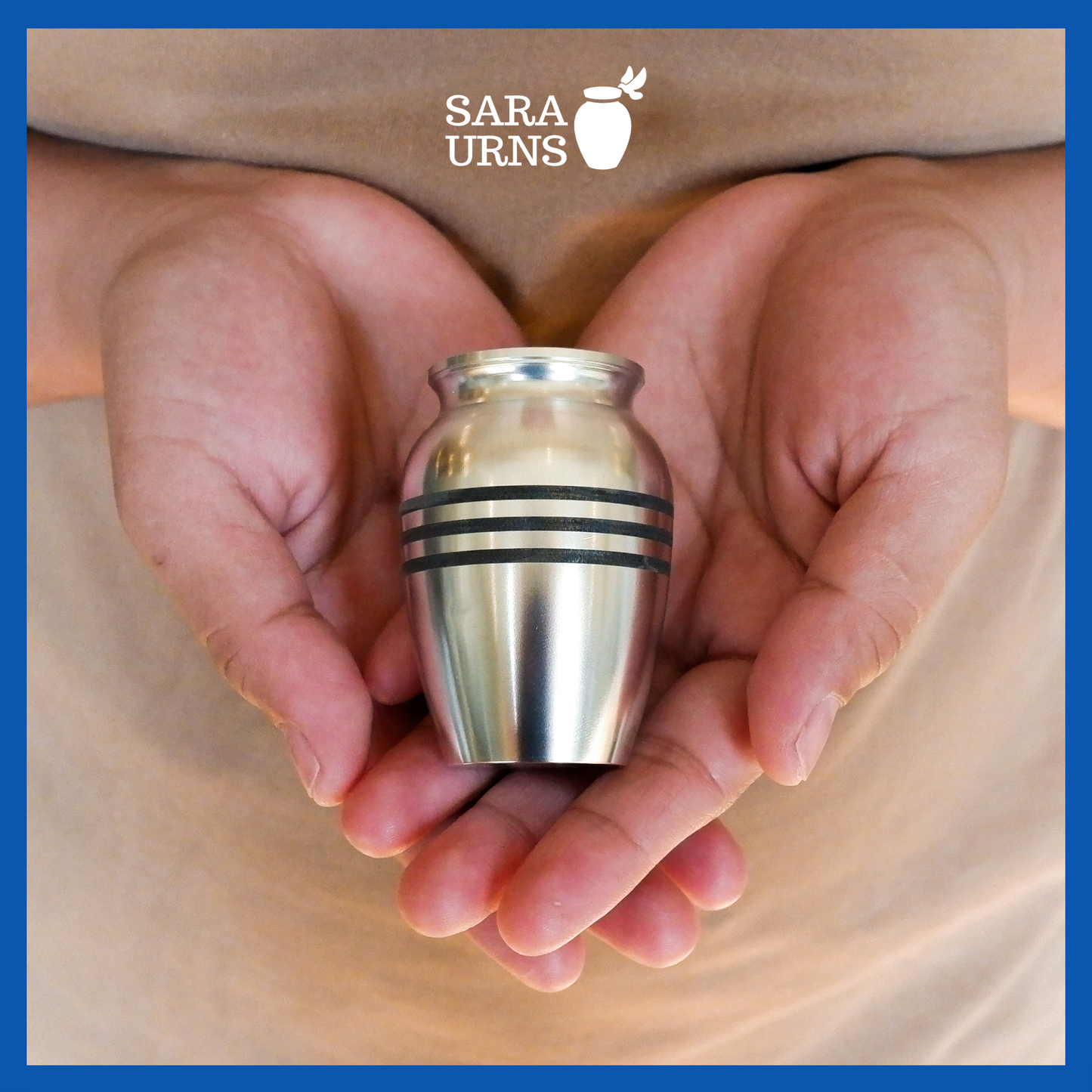 A presentation of a silver alloy metal keepsake urn with three black stripes held by an adult woman with two hands.