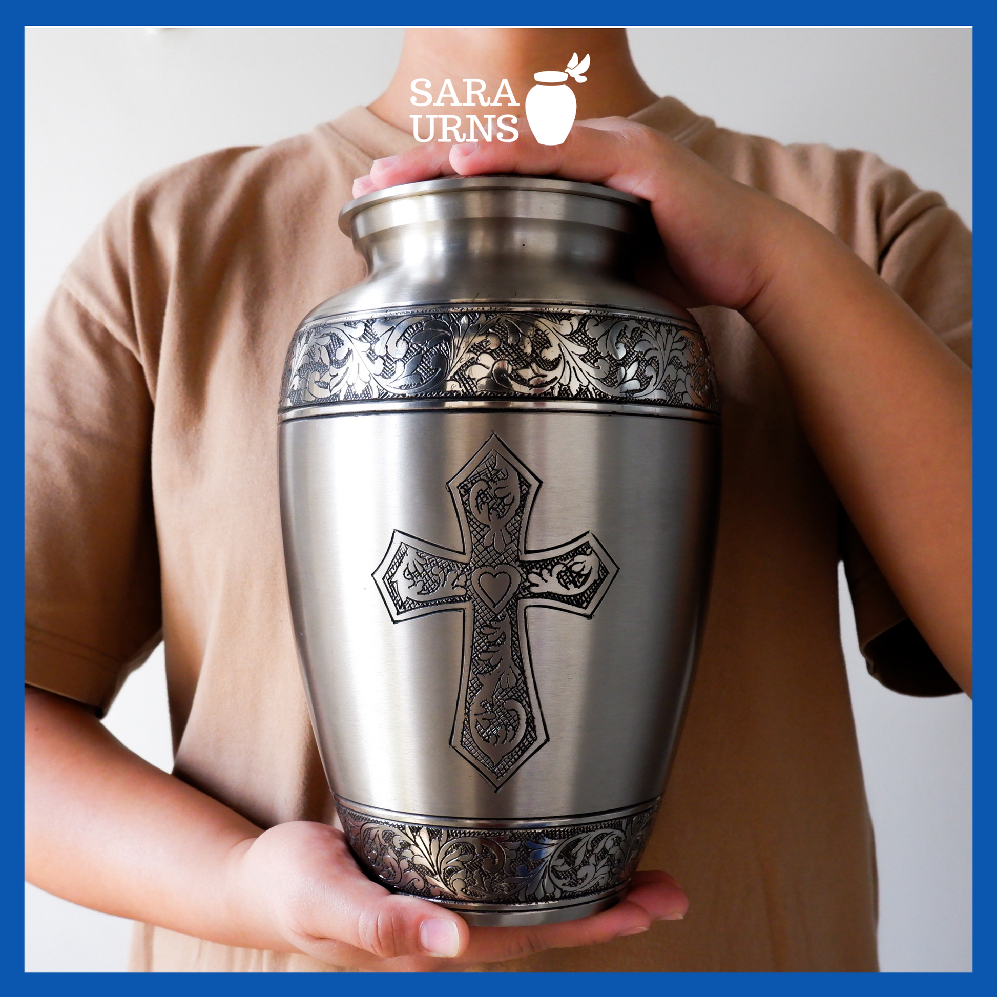 A silver polished brass metal urn with a hand-etched holy cross held by an adult woman with two hands.