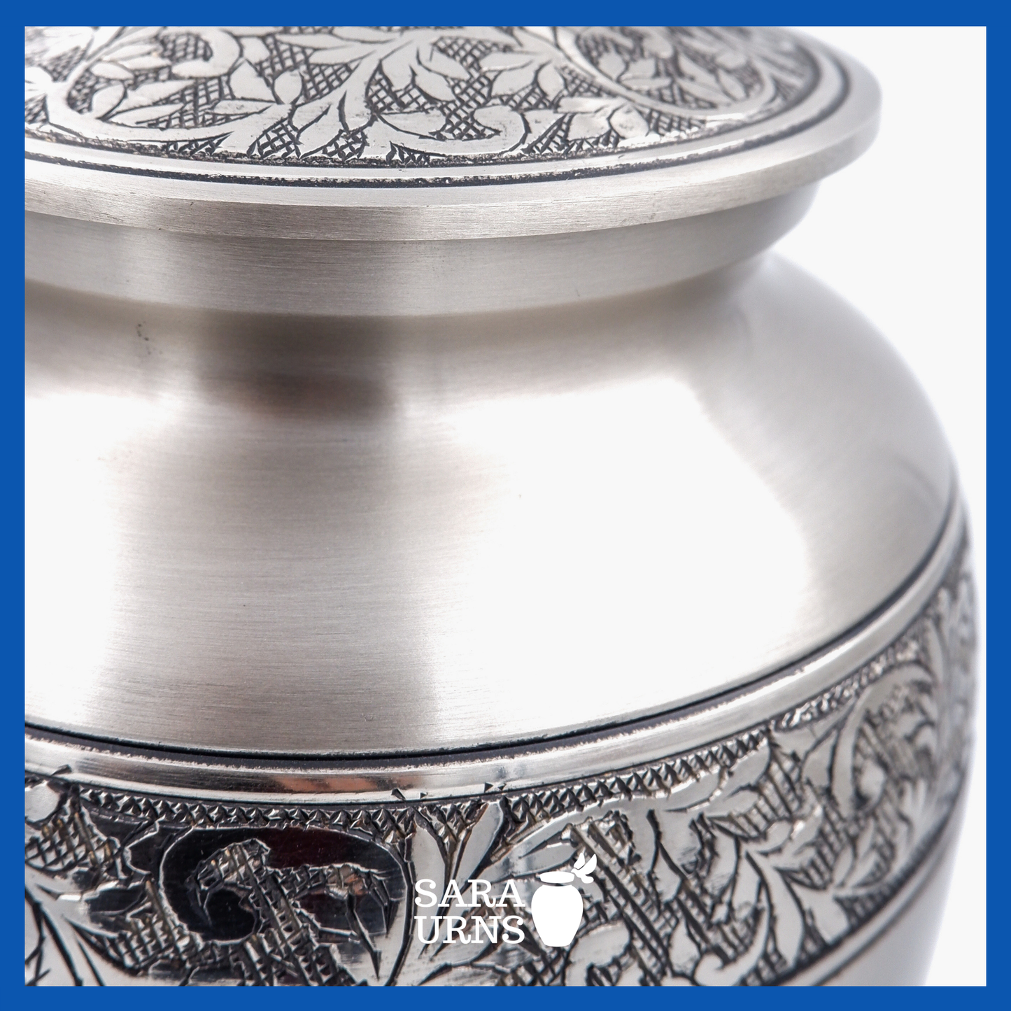 A close-up angle of a silver polished brass metal urn which highlights its hand-etched details on its body and lid.