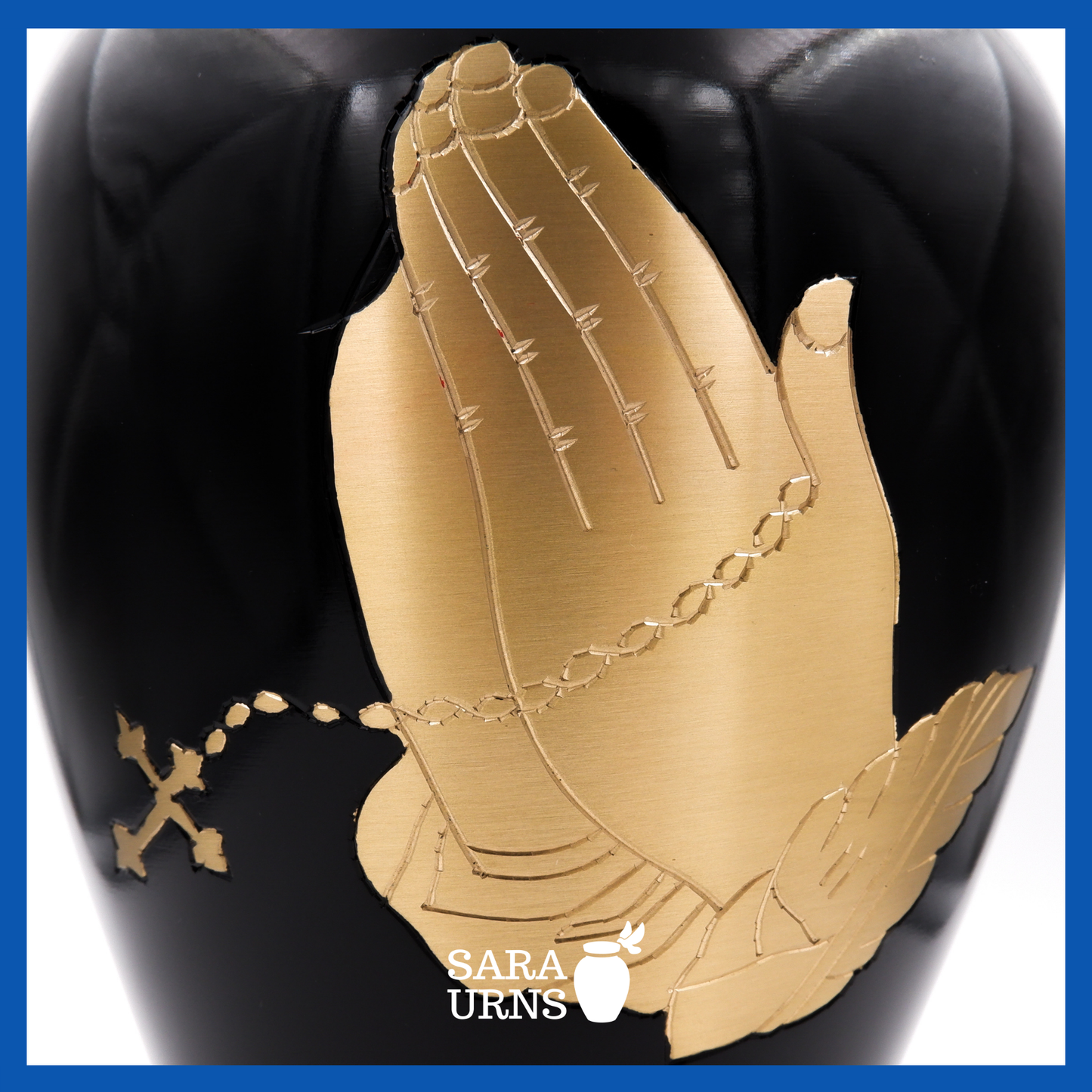A close-up angle of a black polished brass metal urn which highlights its golden hand-etched detail of praying with a rosary.