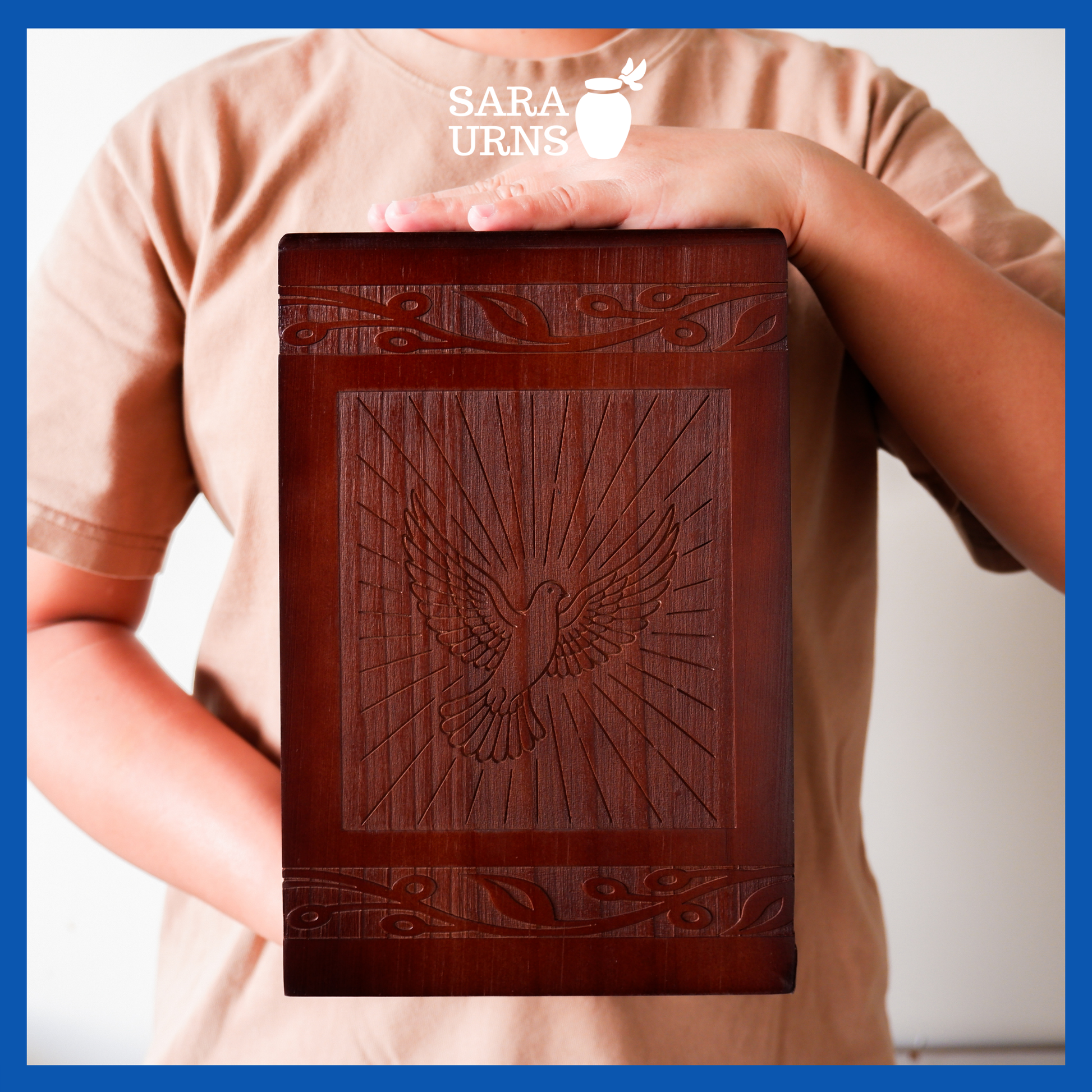 A presentation of a brown pine wooden urn with an intricate engraving of a dove held by an adult woman with two hands.