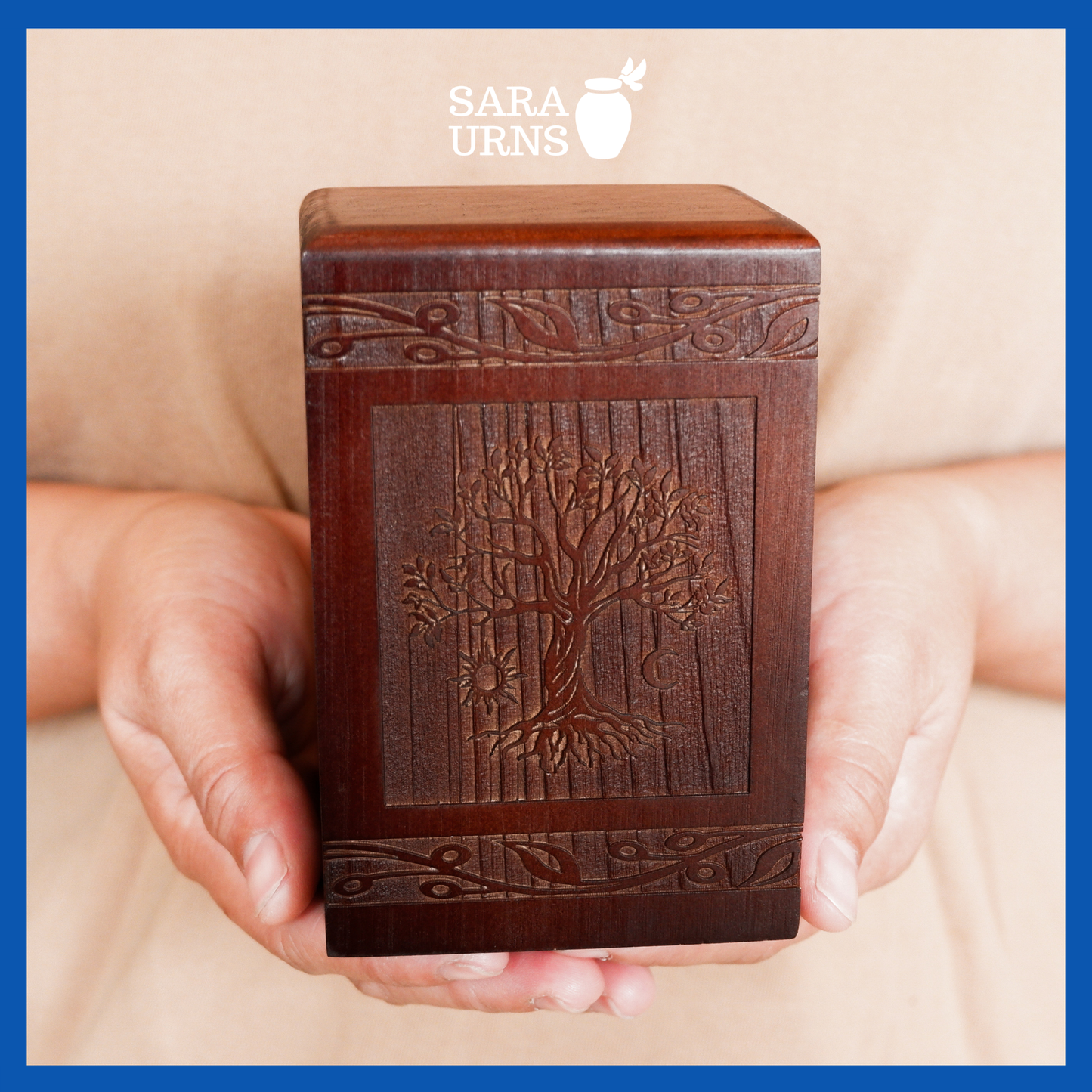 A presentation of a brown pine wooden keepsake urn with an intricate engraving of the tree of life held by an adult woman with two palms.