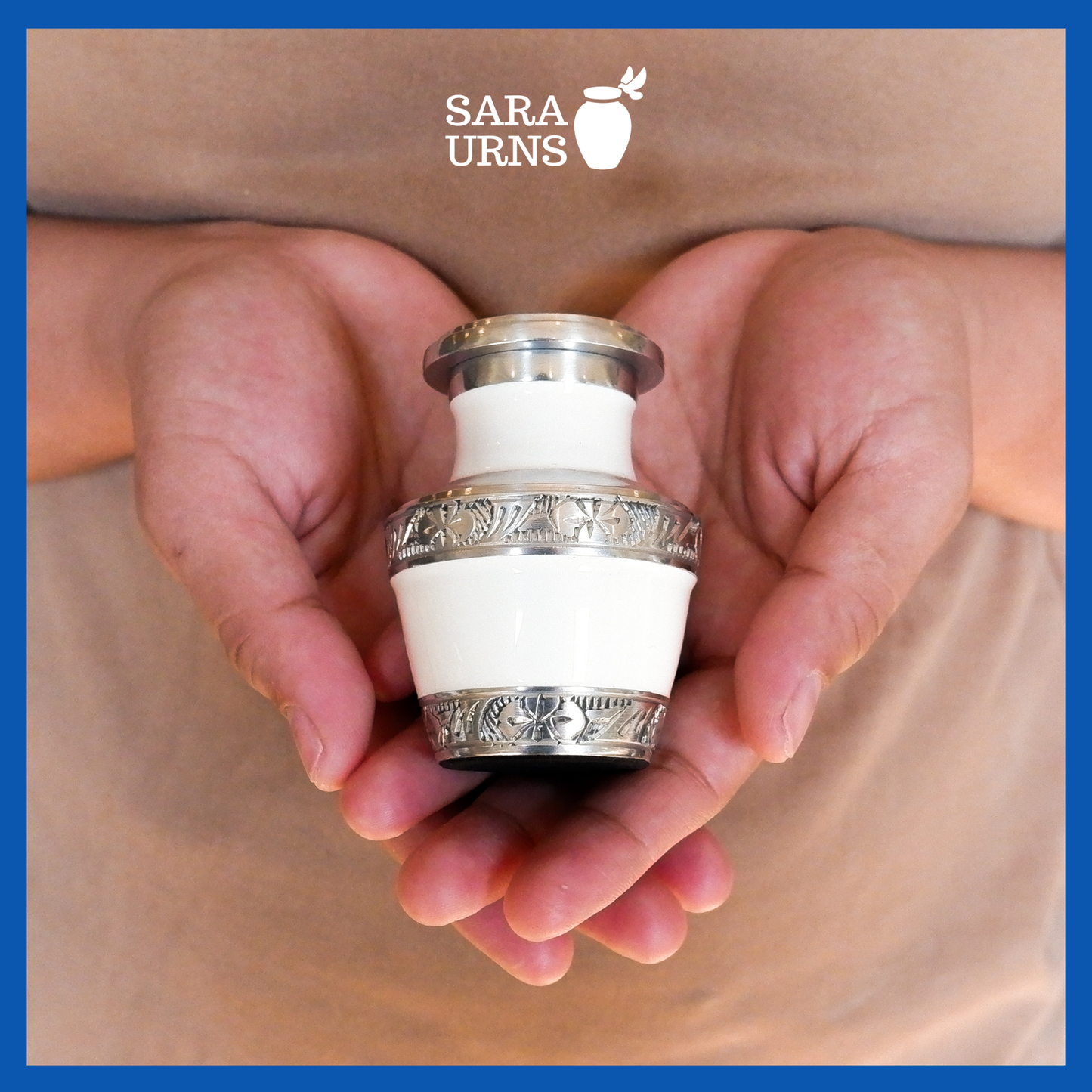A presentation of a white aluminum metal keepsake urn with silver hand-etched designs across the body and lid held by an adult woman with two hands.
