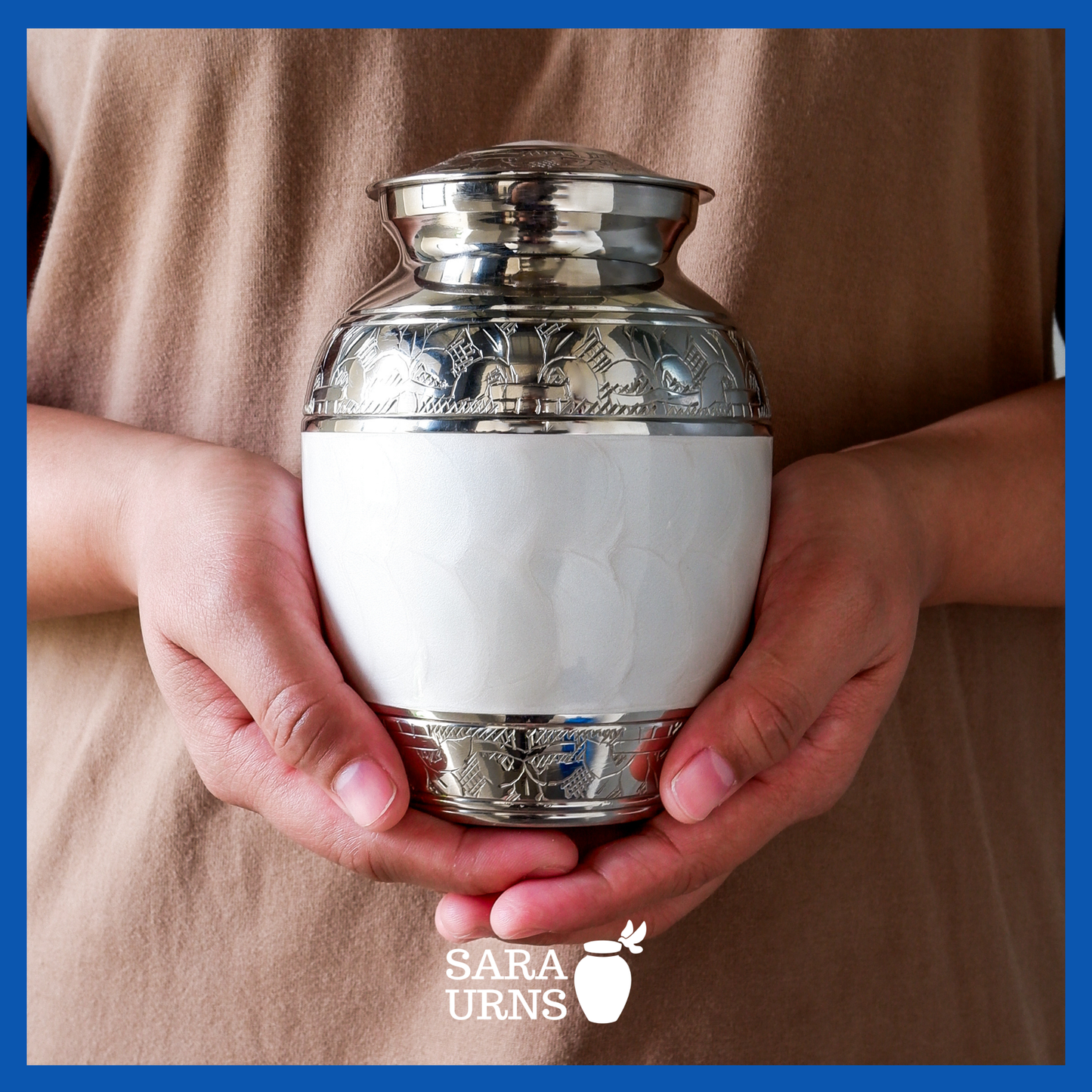 A presentation of a white polished brass metal baby urn held by an adult woman with two hands.