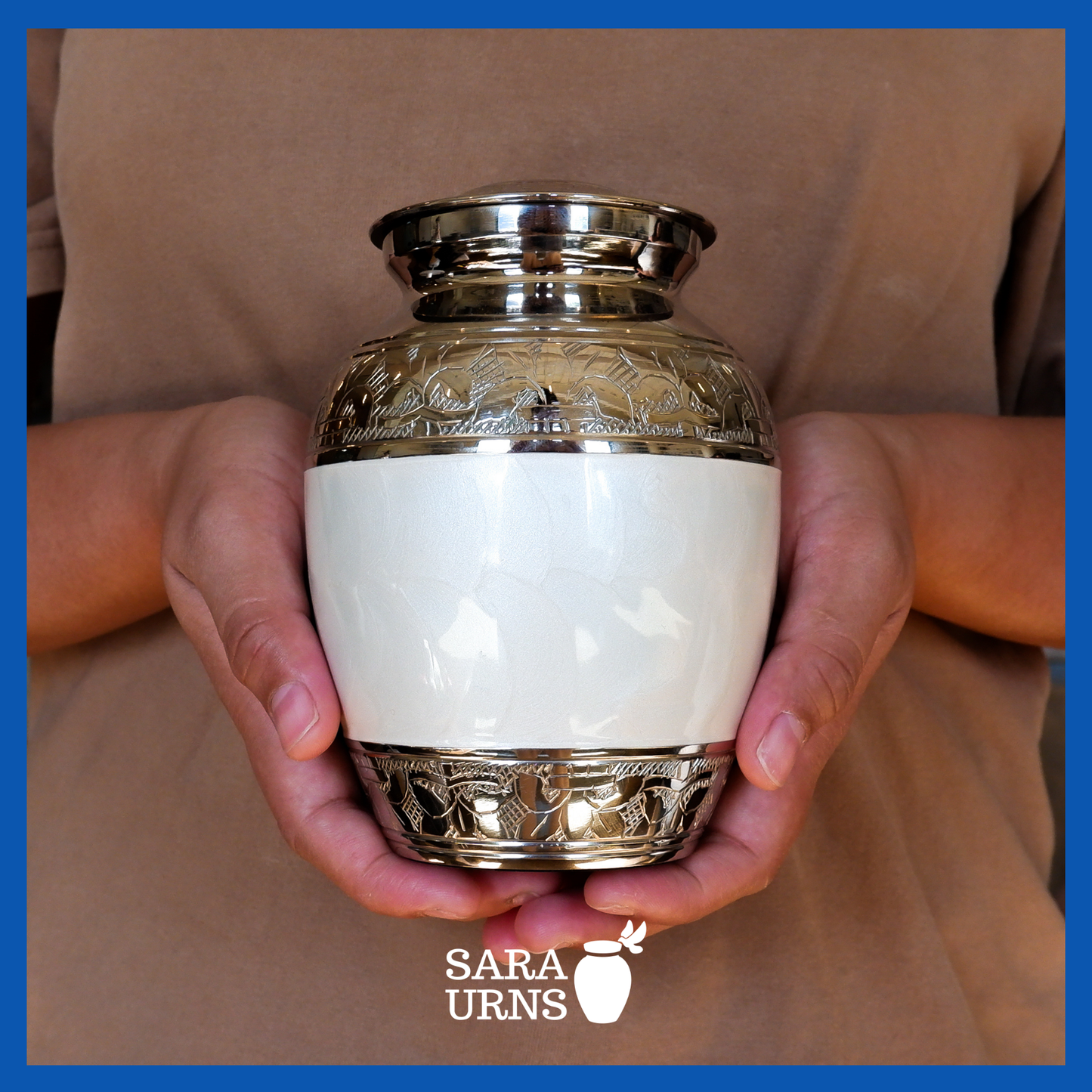 A presentation of a white polished brass metal baby urn held by an adult woman with two hands.
